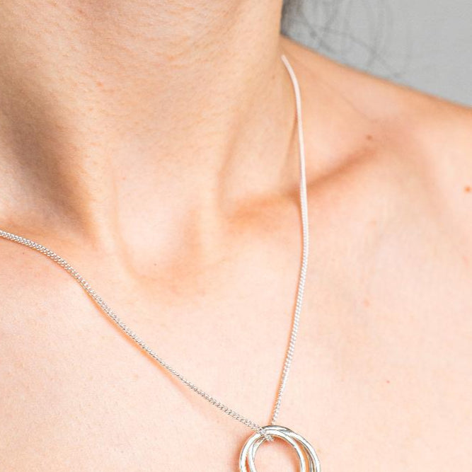 Sterling Silver Necklace with a intertwined Russian Ring Style pendent with a Hammered texture. Worn on a model with side profile.