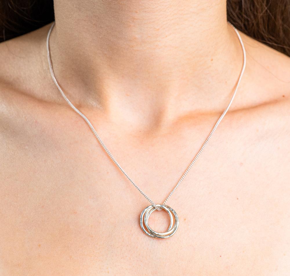 Sterling Silver Necklace with a intertwined Russian Ring Style pendent with a Hammered texture. Worn on a model with front profile.