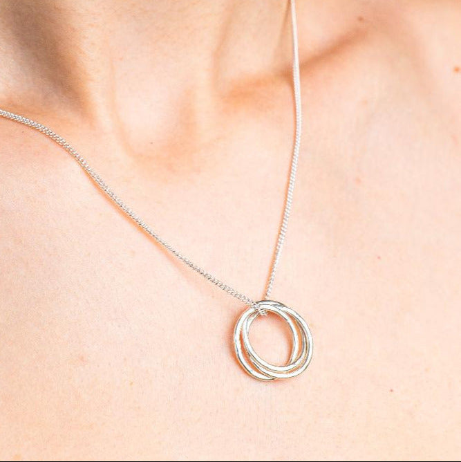 Sterling Silver Necklace with a intertwined Russian Ring Style pendent with a Hammered texture. Worn on a model with side profile.