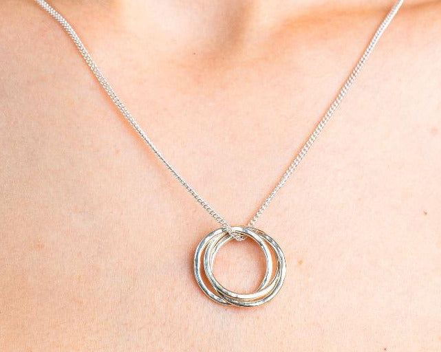 Sterling Silver Necklace with a intertwined Russian Ring Style pendent with a Hammered texture. Worn on a model with front profile.