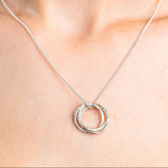 Sterling Silver Necklace with a intertwined Russian Ring Style pendent with a Hammered texture. Worn on a model with front profile.